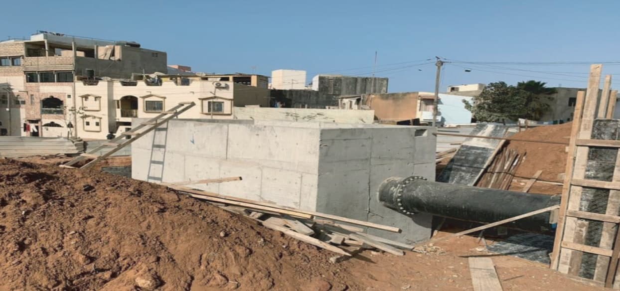 Regard en béton coulé en place, raccordé à une conduite en fonte, au milieu d'un quartier de Dakar.