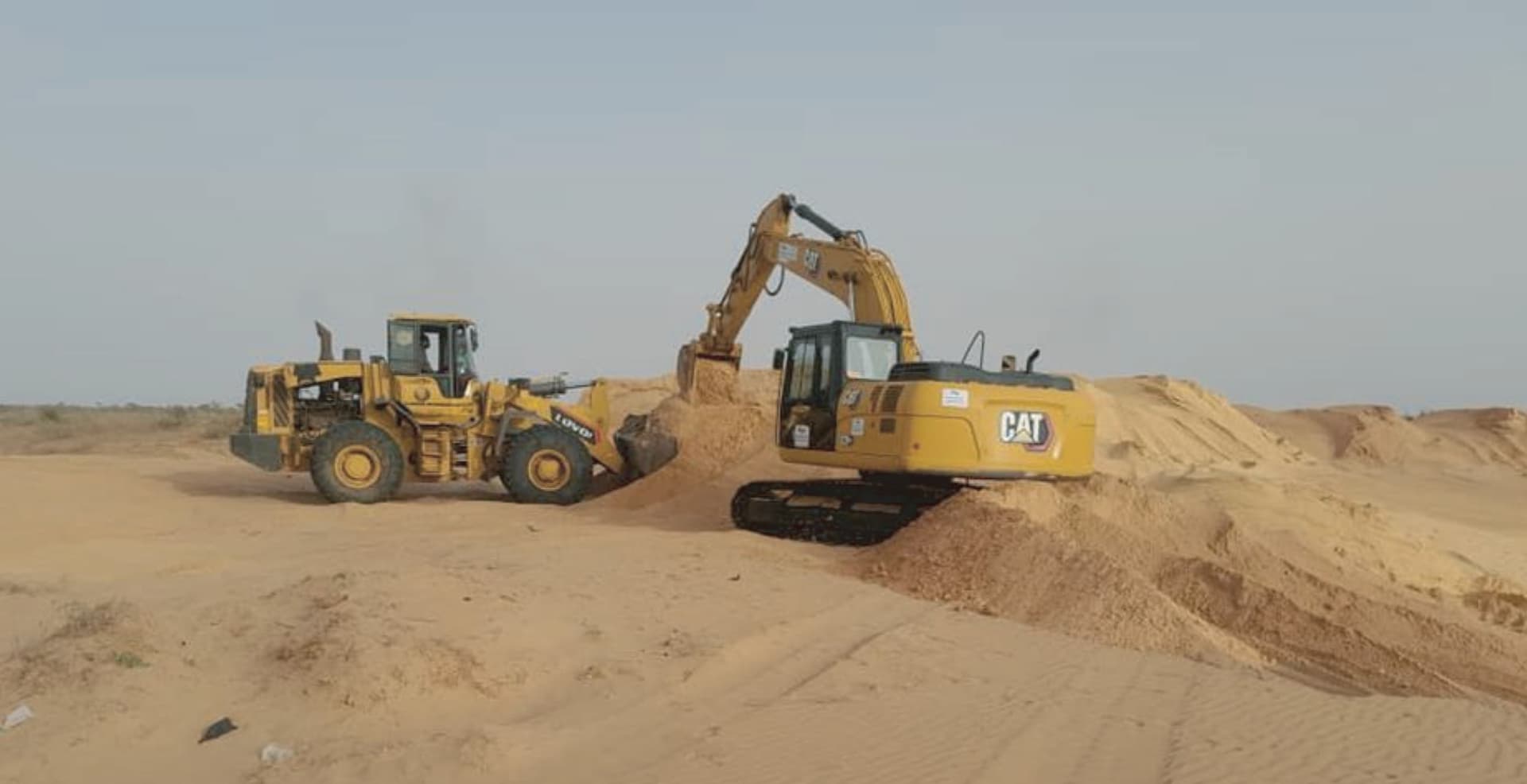 Une chargeuse et une pelle hydraulique CAT terrassent un remblai de sable sur un chantier.